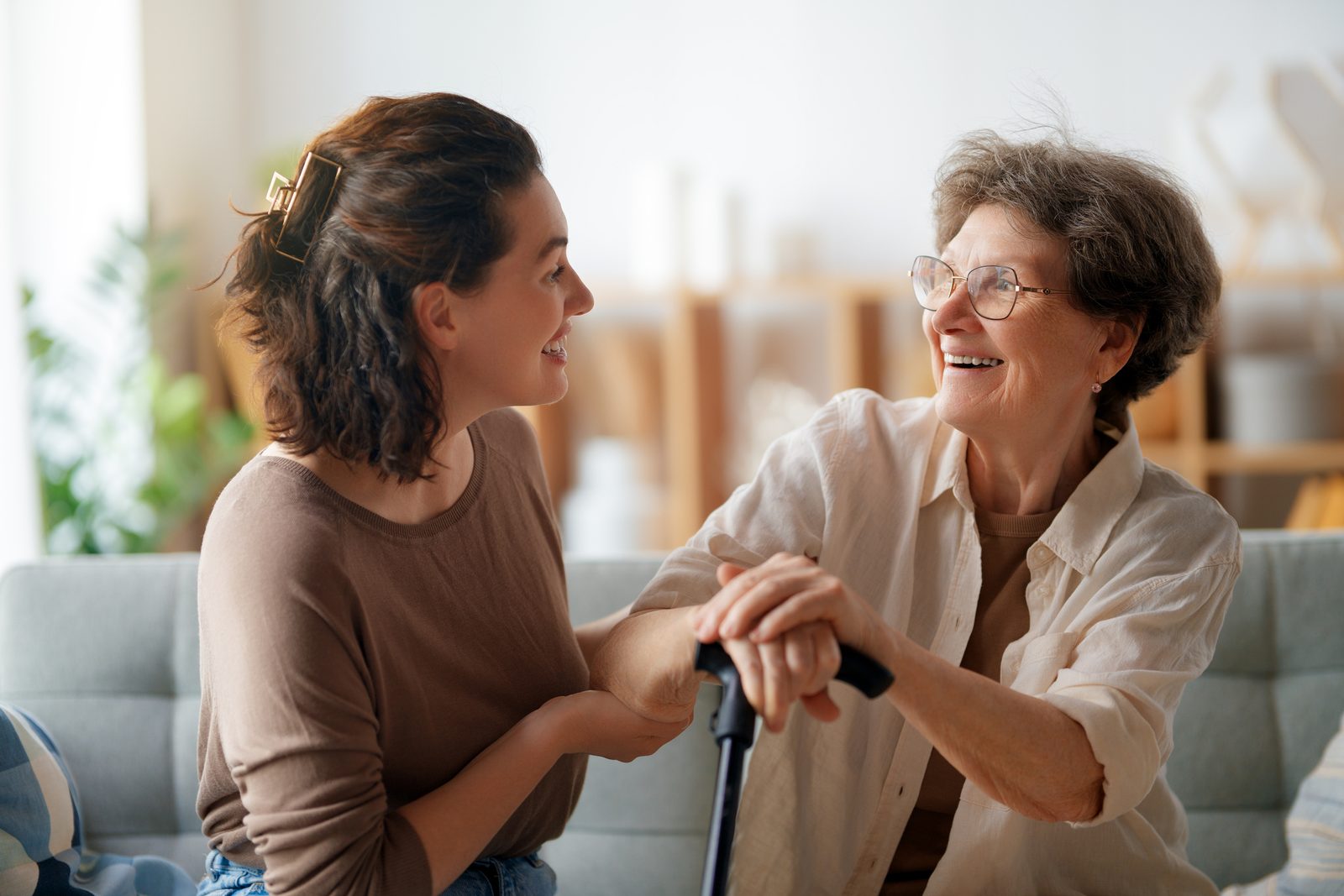A younger woman and an older woman sitting close together at home, holding hands and smiling at each other